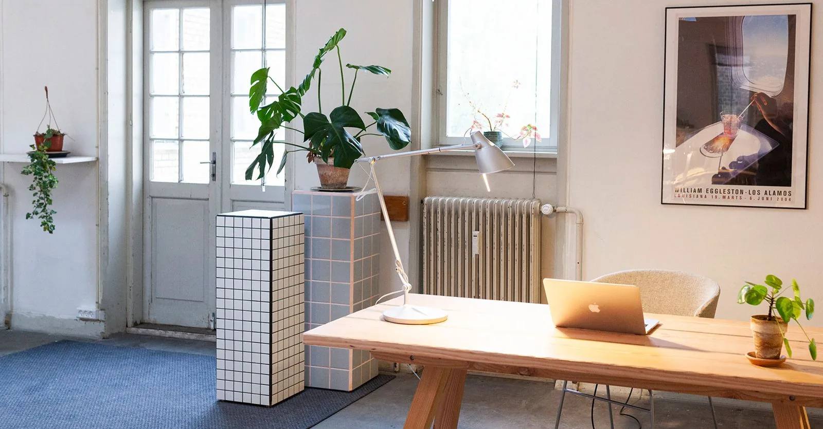 A light wooden desk by the window, with a lamp and plants.
